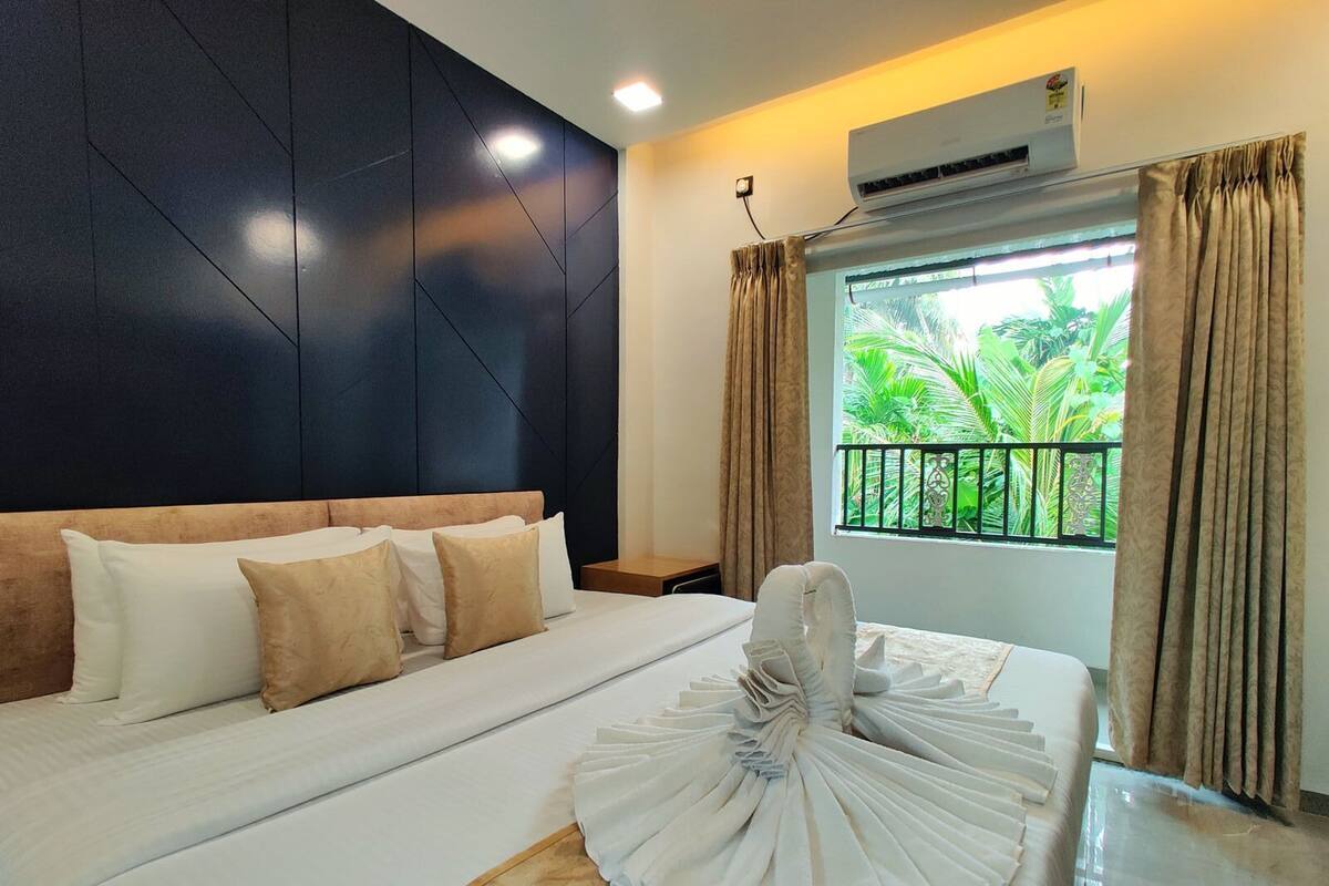 A hotel room with a large bed, a headboard, a window with curtains, and an air conditioning unit.