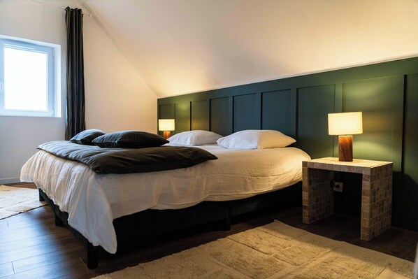 Een slaapkamer met een bed, twee nachtkastjes met lampen, een raam met gordijnen en een houten vloer.