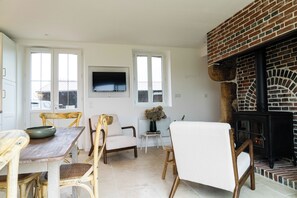 Een eetgedeelte met een houten tafel en stoelen, een televisie die aan de muur is bevestigd, en een open haard met een bakstenen omlijsting.
