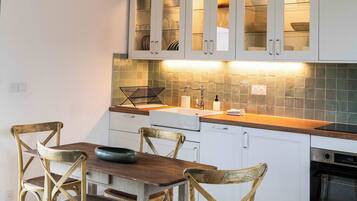 Een moderne keuken met witte kasten, een houten eettafel en rieten stoelen.