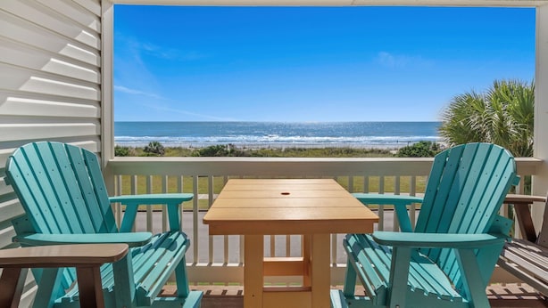 Un espacio de estar techado al aire libre con una mesa y sillas, con vistas a una playa y al océano, con palmeras.