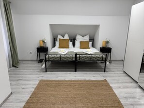 Een slaapkamer met een bed, twee nachtkastjes, een geweven vloerkleed en een groen gordijn.