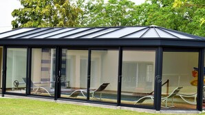 A glass-enclosed structure with a roof, likely a sunroom or conservatory, adjacent to a building with a visible interior. - Tourangelle House with Indoor Pool, Wifi, Garden (Assay)