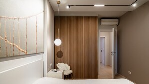 A modern bedroom with a bed, a bedside table, a chair, a hanging light fixture, and a wooden panel wall.