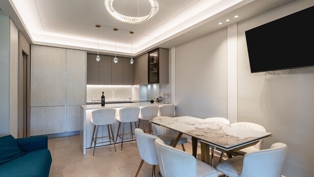 A modern kitchen with a marble countertop, white bar stools, and a dining table with chairs.