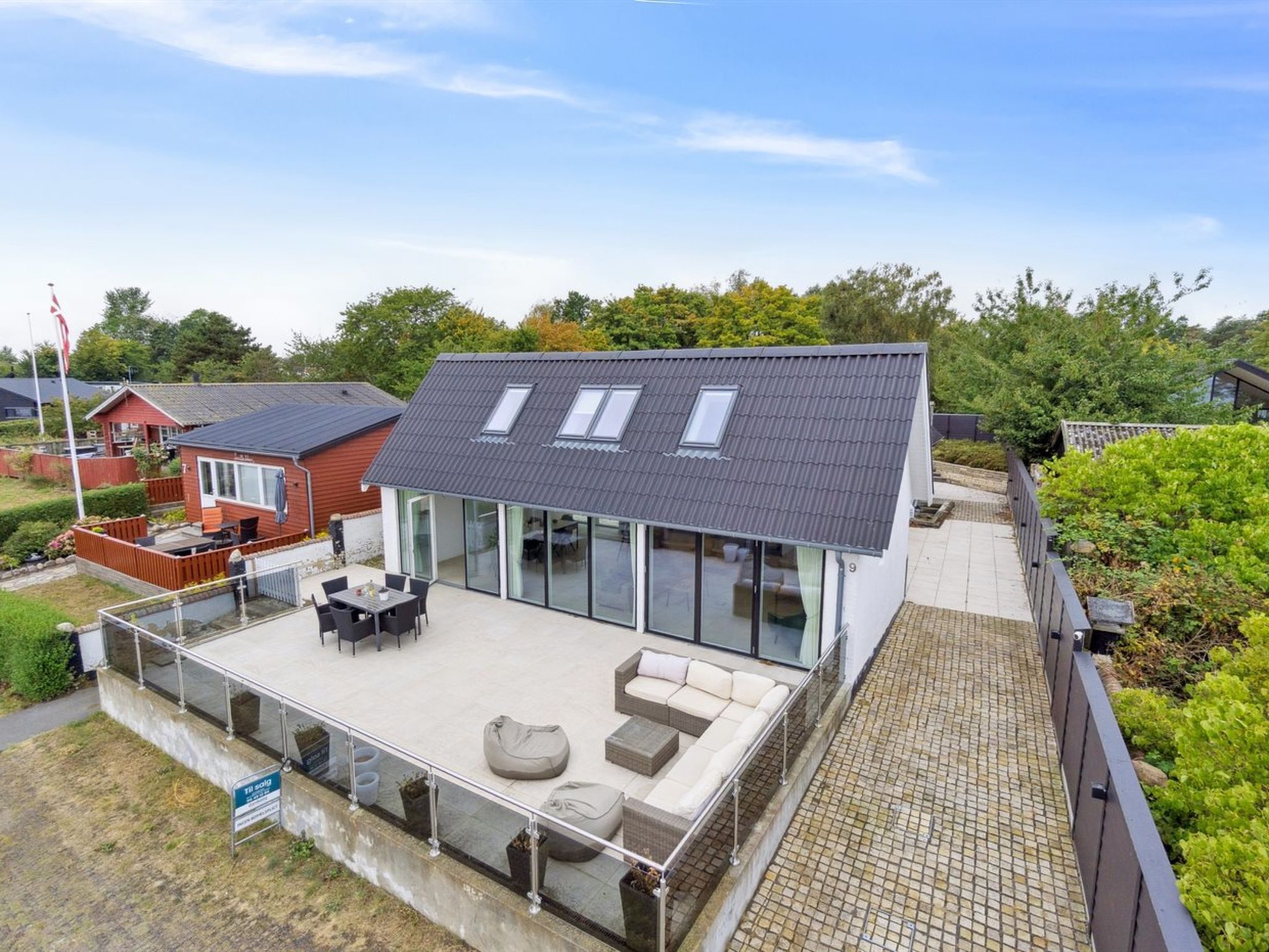 Ein modernes Haus mit großem Glasbalkon, einer flachen Dachkonstruktion und einer gepflasterten Terrasse.