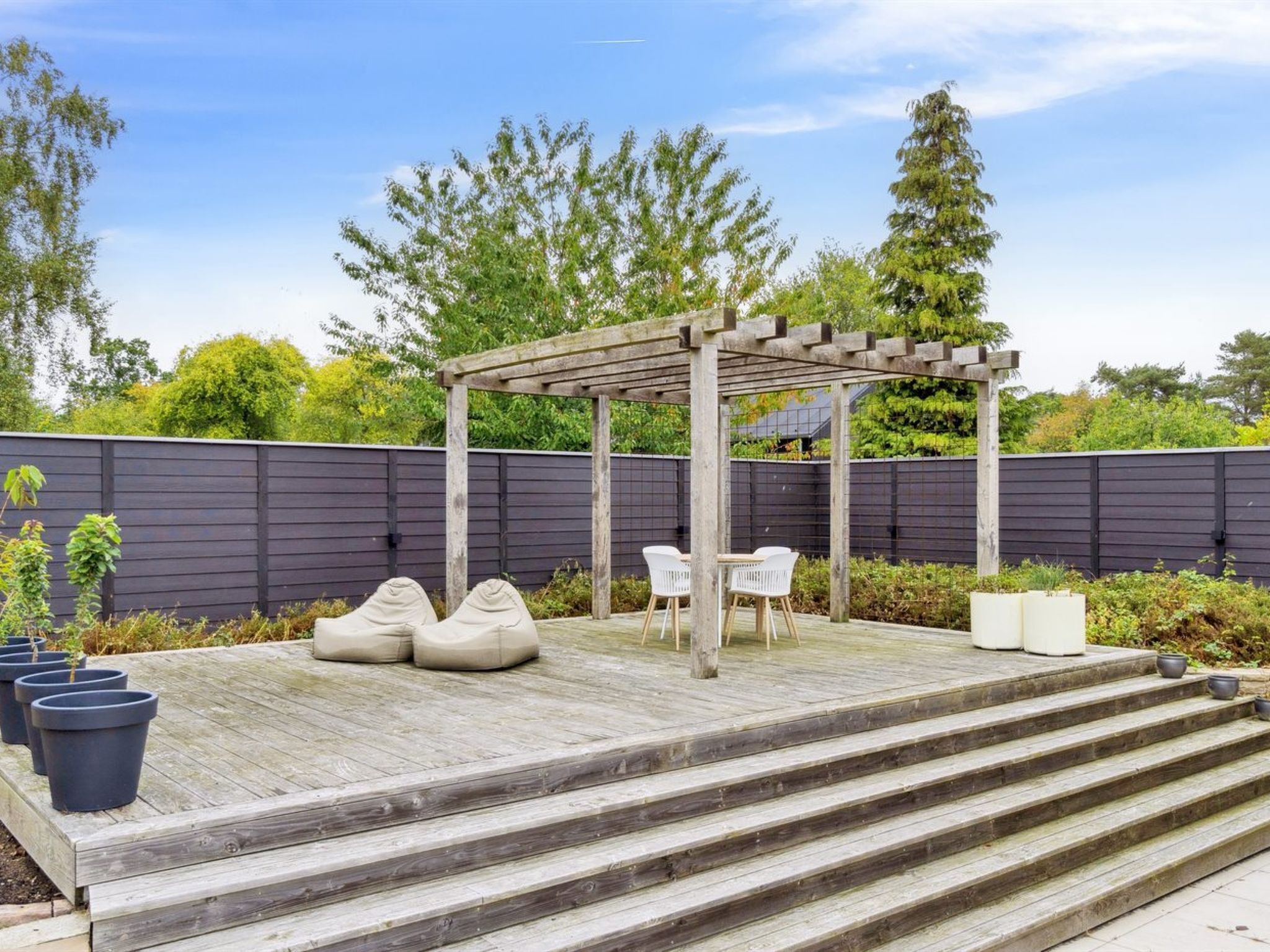 A wooden deck with a pergola, outdoor seating, and steps leading up to the deck.