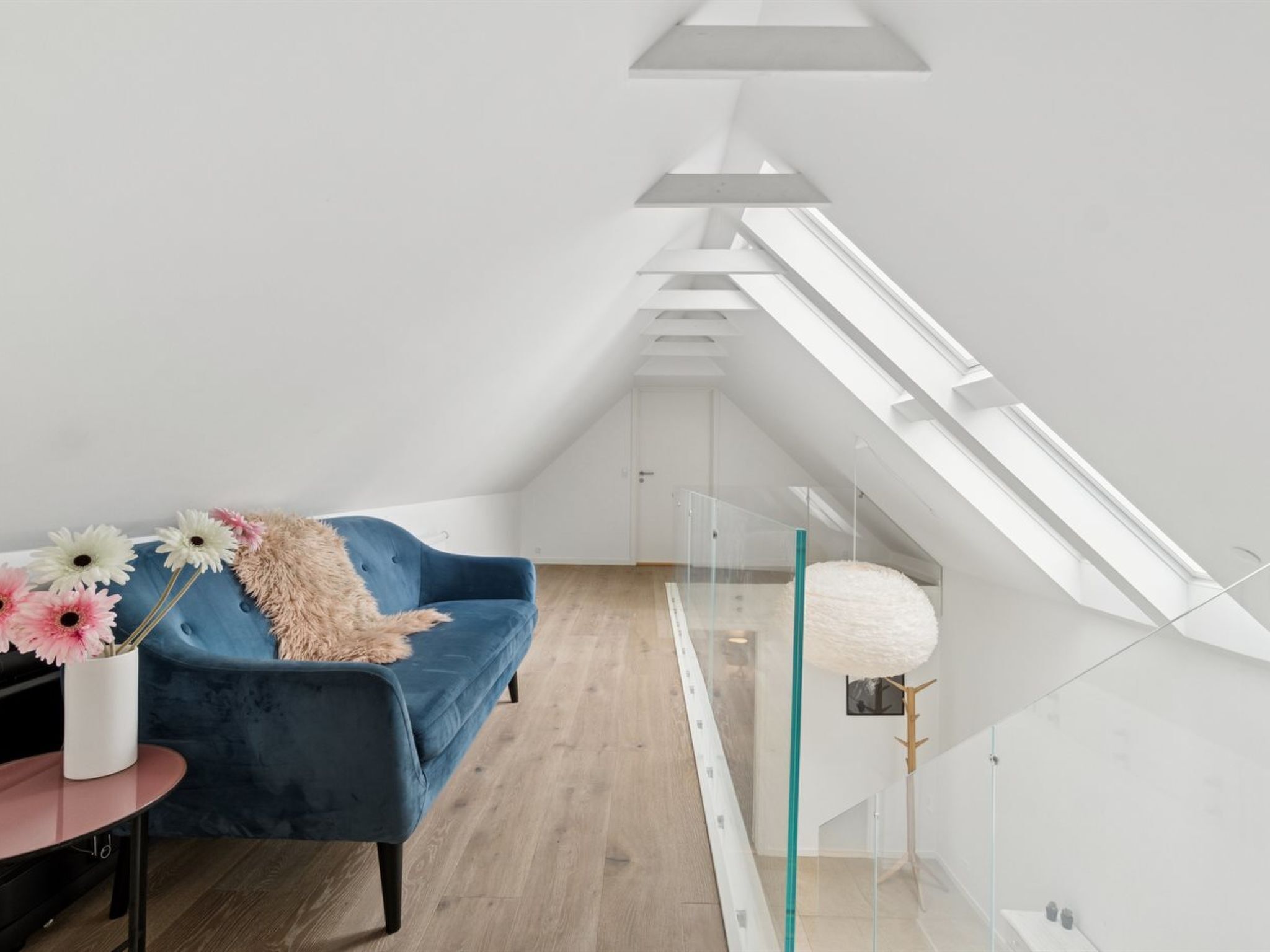 Une chambre de style loft moderne, dotée d’une lucarne, d’un canapé bleu et d’une rambarde en verre.