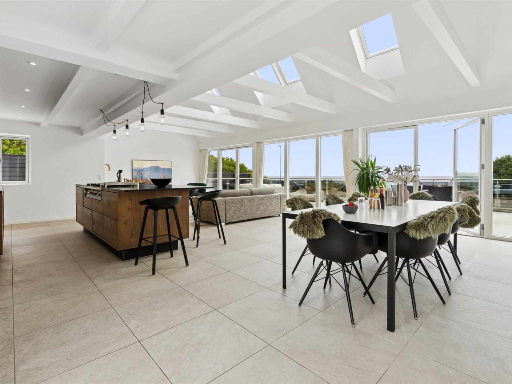 A modern kitchen with a central island, dining area with chairs, and large windows offering a view.