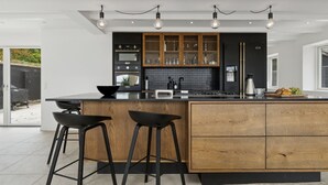 Cocina moderna con una isla central, taburetes de bar, armarios de madera e iluminación colgante.