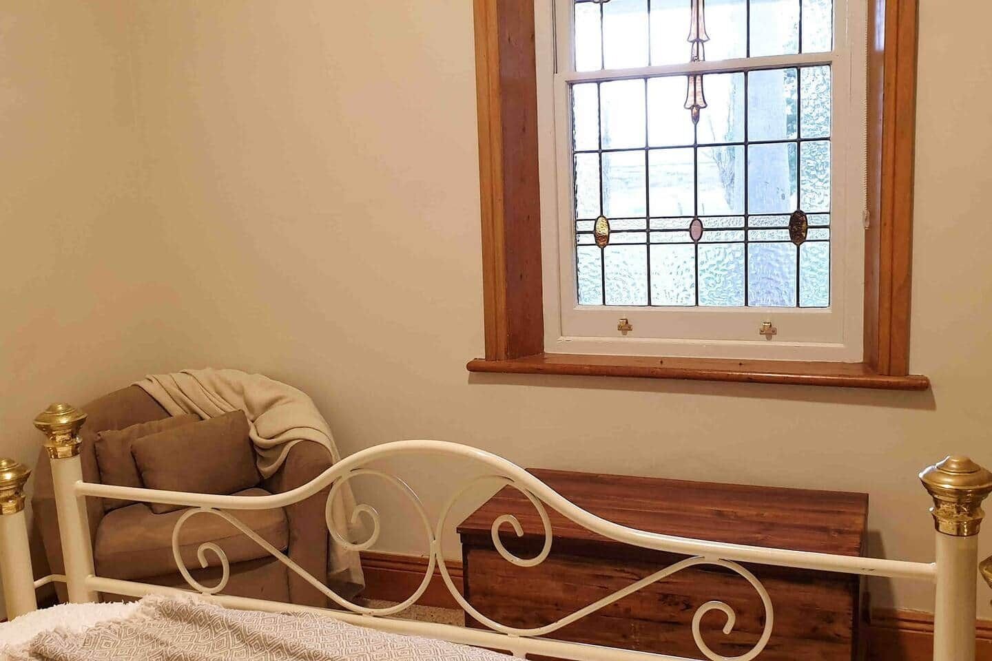 Une chambre à coucher avec un lit en métal blanc, une tête de lit en bois, une fenêtre avec un cadre en bois et une table de chevet avec une lampe.