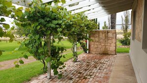 A covered outdoor area with a brick floor, a stone wall, and a pergola with climbing plants.