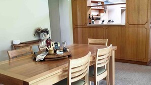 A wooden dining table with chairs, a tray with glasses and condiments, and a kitchen area in the background.