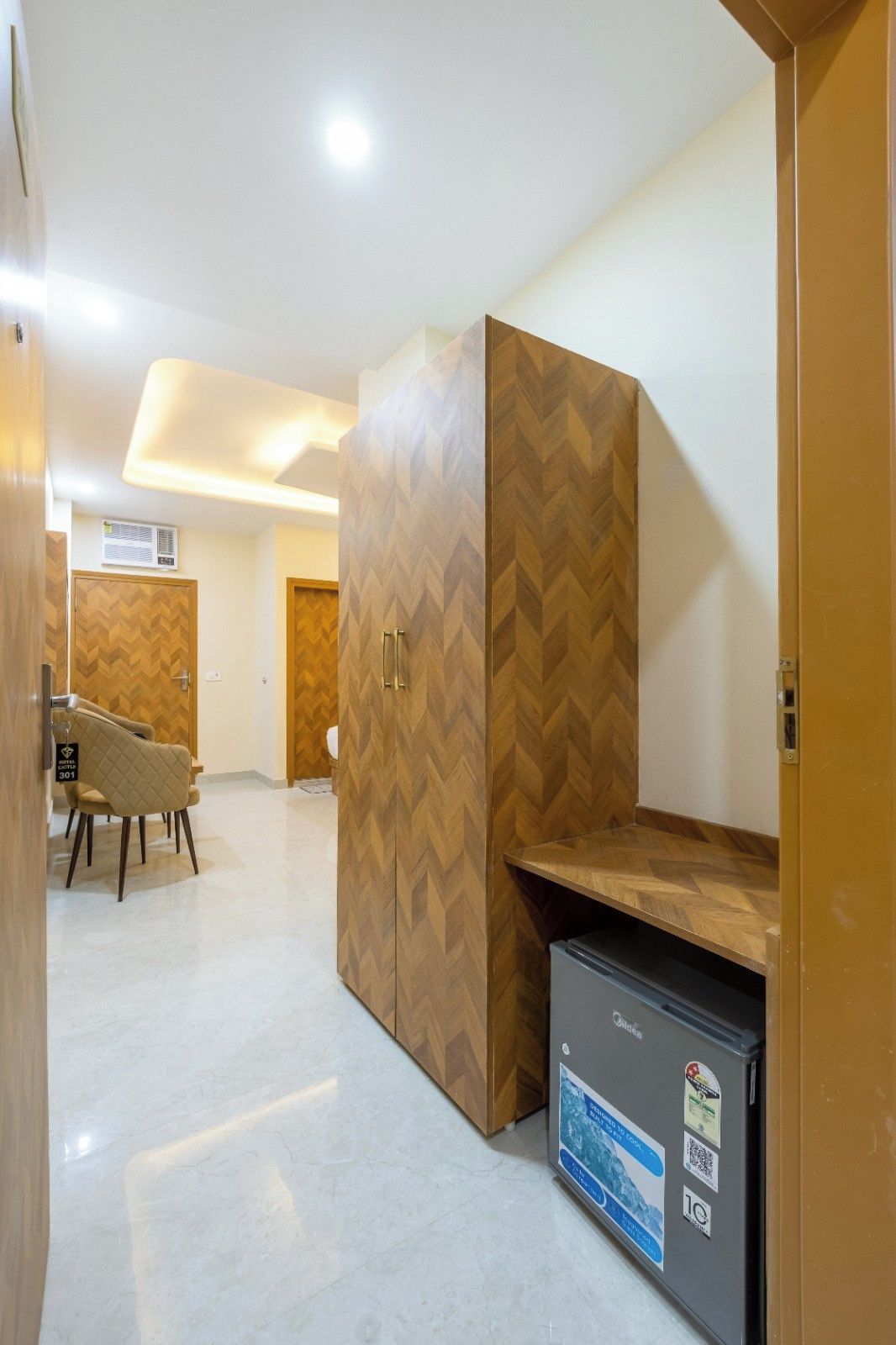 A hotel room with a herringbone-patterned wardrobe, a small desk, and a refrigerator.