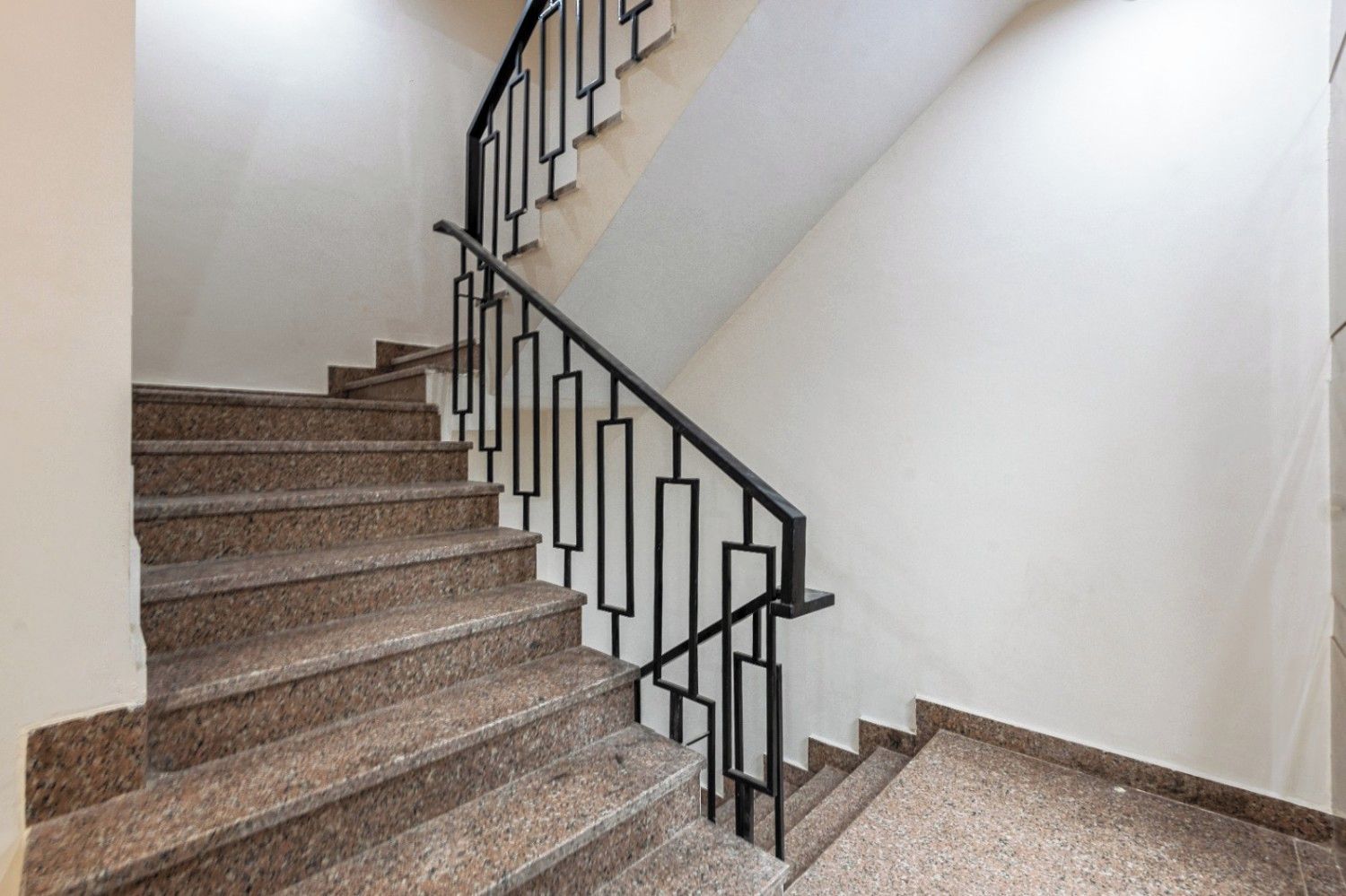 Una escalera con escalones de granito y barandilla de metal negro.