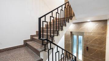 A staircase with a geometric railing design, leading to a landing with a glass door and a marble wall.