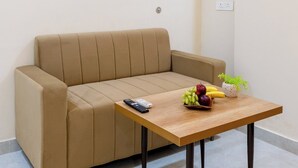 Sala de estar minimalista com um sofá bege, uma mesa de centro de madeira com frutas, um controle remoto e uma tomada na parede.
