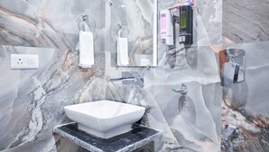 A bathroom with a marble backsplash, a white sink, and modern fixtures including a handheld showerhead and a soap dispenser. - Hotel Yashobhoomi Inn (New Delhi)