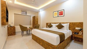 Quarto de hotel com cama, duas cadeiras, escrivaninha e uma mesinha.