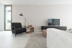 A modern living room with a sofa, a TV, a lamp, and a small wooden side table.