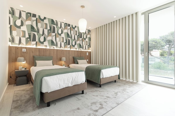 A modern bedroom with two beds, a geometric wall art piece, a large window with curtains, and a light fixture.