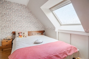 A bedroom with a sloped ceiling, a skylight, a bed with a pink quilt, a wooden nightstand, and two stuffed toys. - Bed and Breakfast 'Le Jardin Aux Oiseaux' with Wi-Fi (Saint-Jouan de l'Isle)