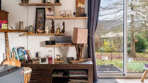 A room with a glass door leading to a garden, shelves with books and decorative items, and a drum set.