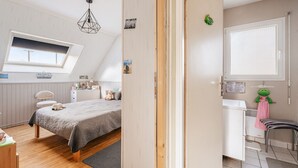 A bedroom with a bed, a desk, a chair, a window, and a bathroom with a towel rack.