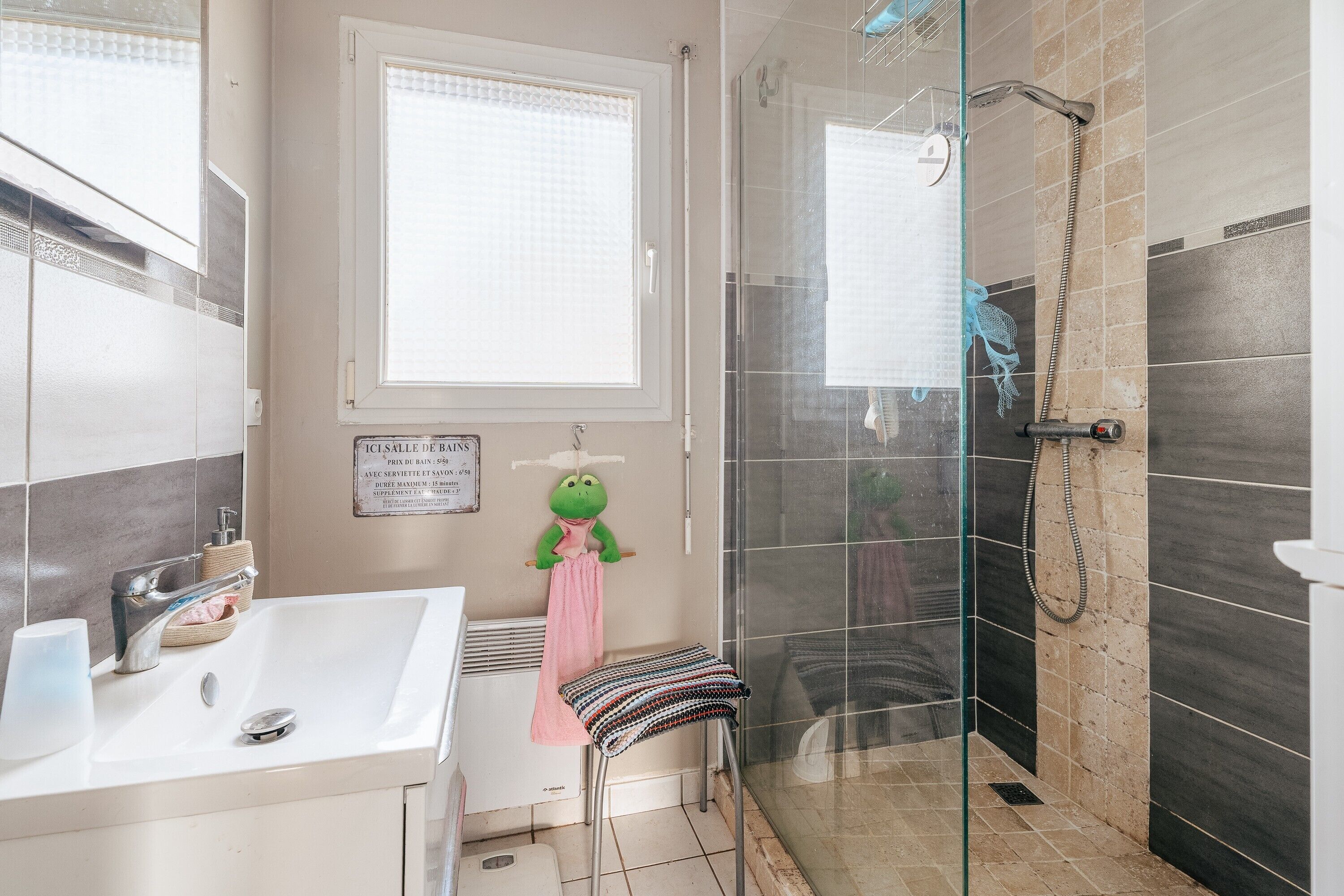 Une salle de bain équipée d’un lavabo, d’un porte-serviettes, d’une douche avec une porte en verre et d’une fenêtre.