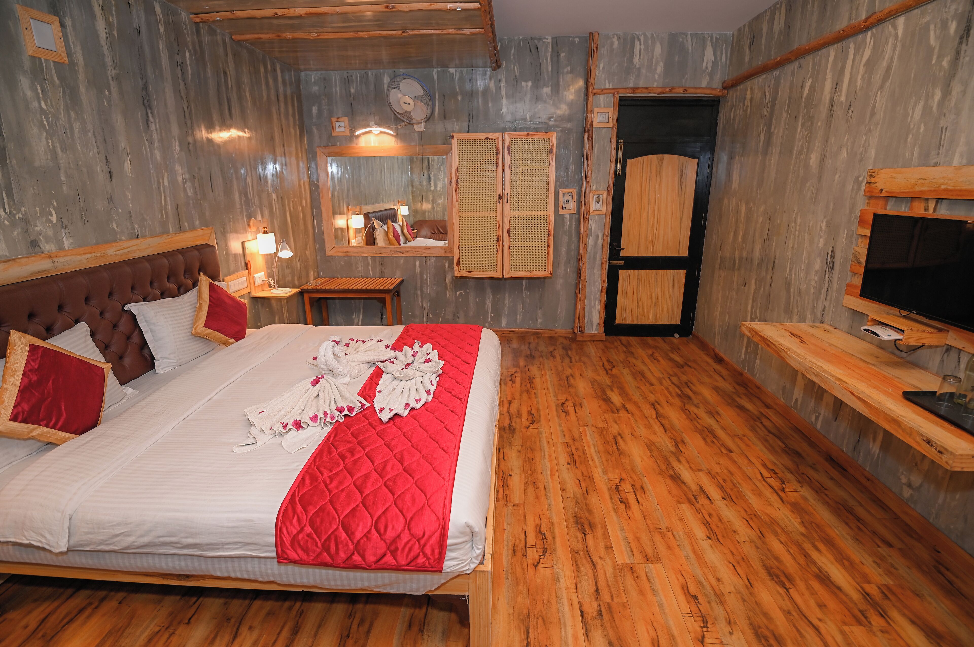 Quarto com uma cama grande, piso de madeira, espelho, guarda-roupa e televisão.