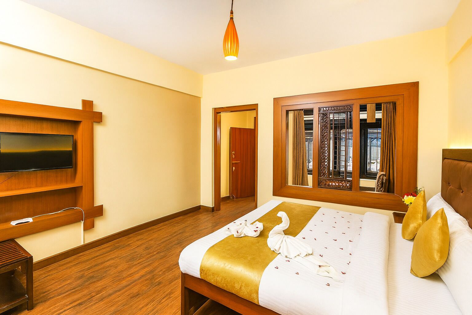 Een hotelkamer met een groot bed, een flatscreen televisie aan de wand, een houten vloer en een raam met gordijnen.