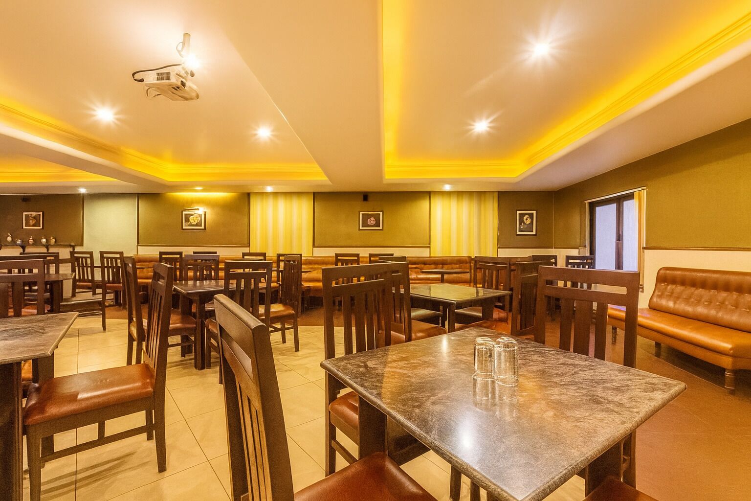 Un restaurant spacieux, doté de nombreuses tables et de banquettes, d’un projecteur au plafond et d’un éclairage chaleureux.
