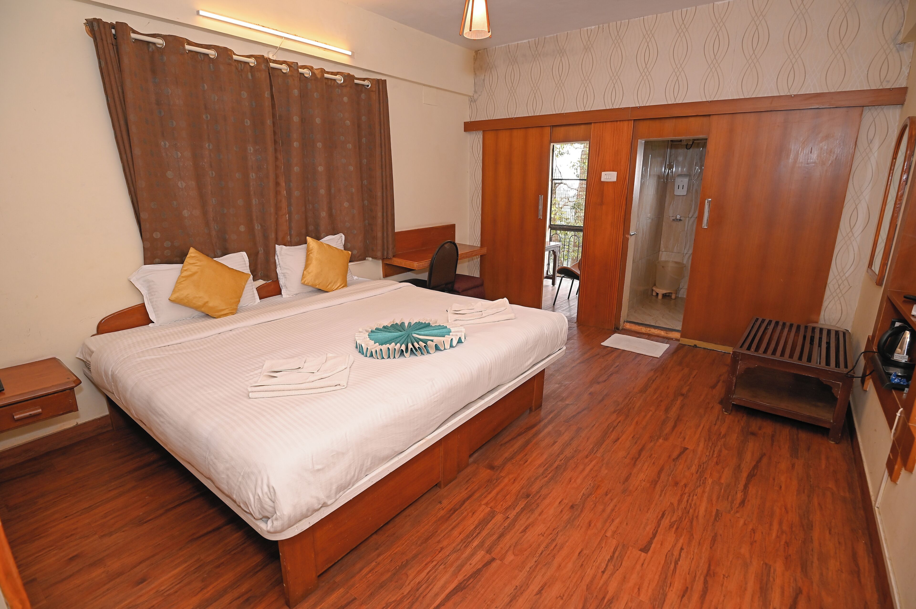 A bedroom with a large bed, wooden floor, a desk, and a sliding door to a balcony.