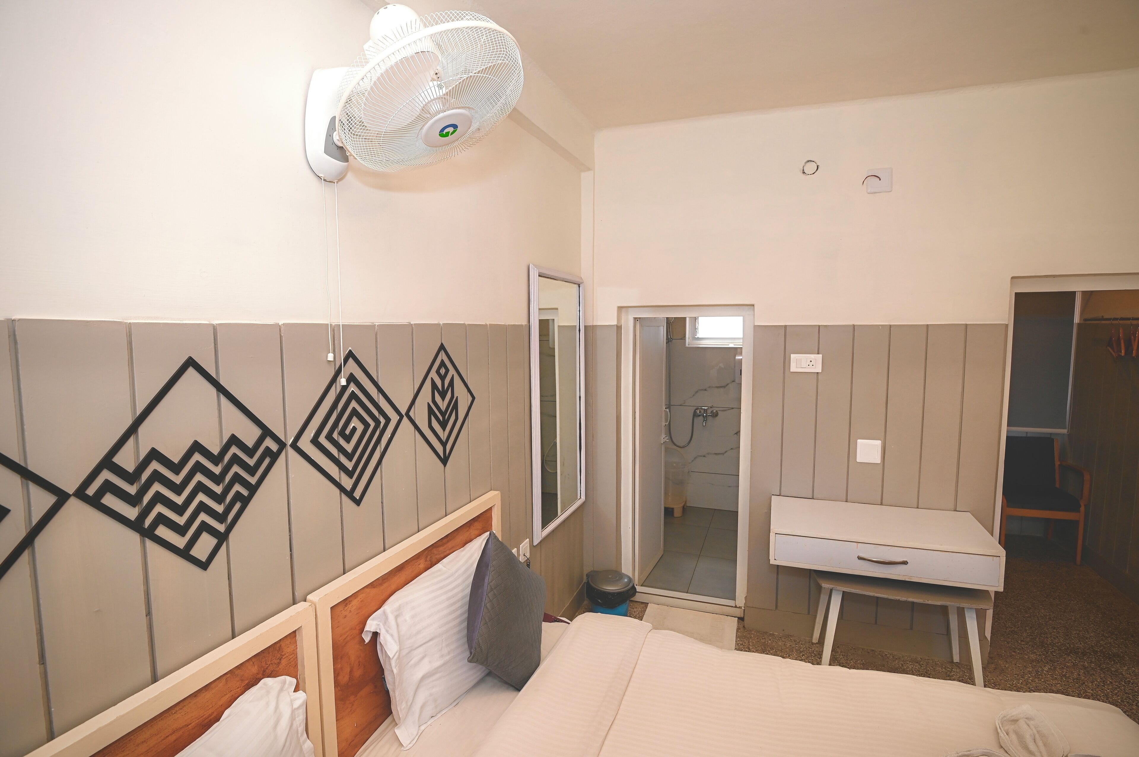 Ein Hotelzimmer mit Bett, Nachttisch, Spiegel, Ventilator und Duschbereich.