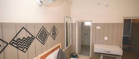 A hotel room with a bed, a bedside table, a mirror, a fan, and a shower area.