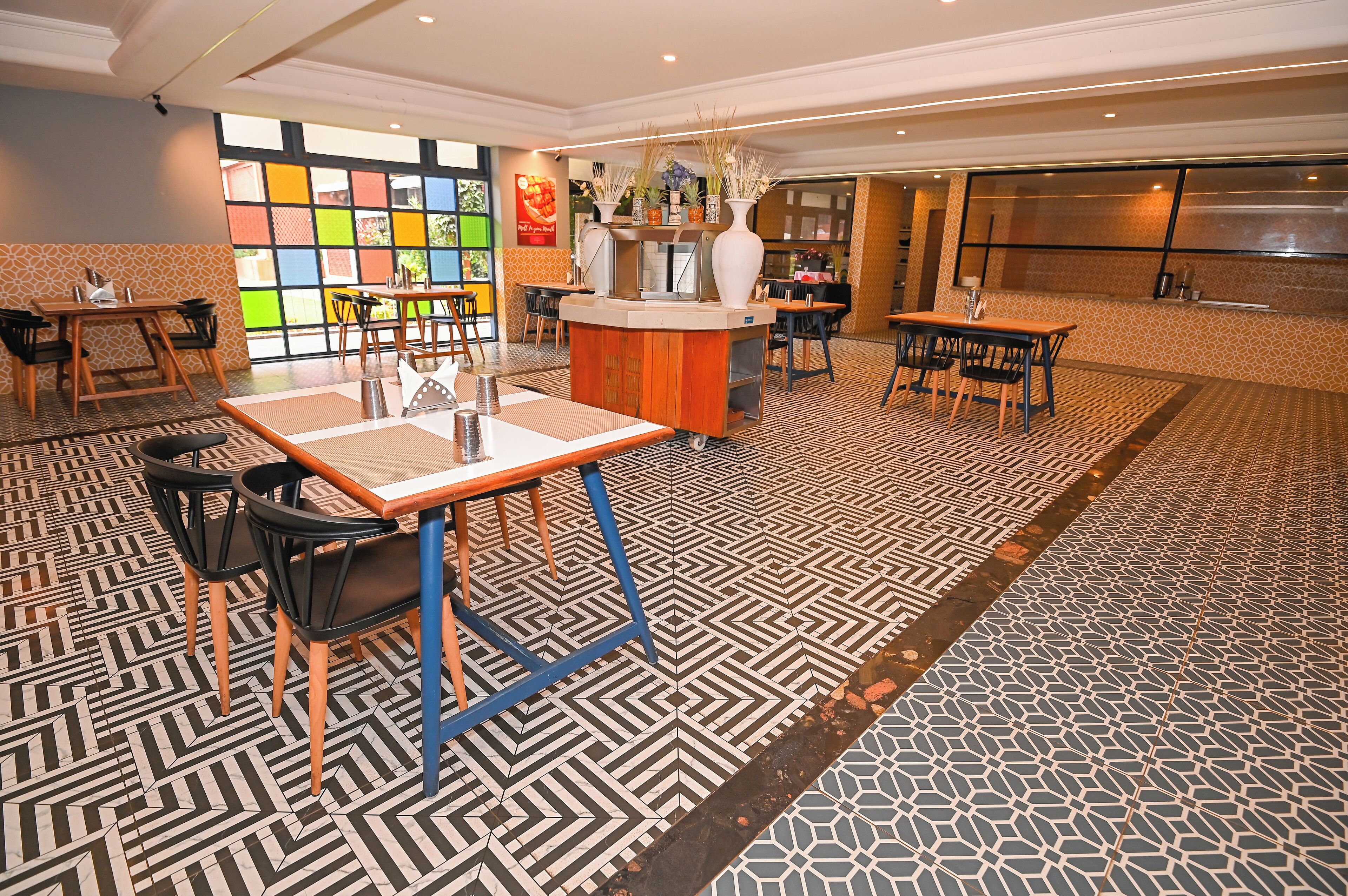 A hotel lobby with a central reception desk, multiple seating areas, patterned flooring, and a colorful wall with a fruit display.
