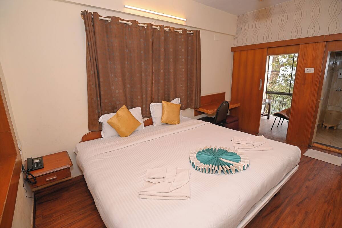A neatly made bed with pillows, a bedside table with a phone, and a window with curtains.