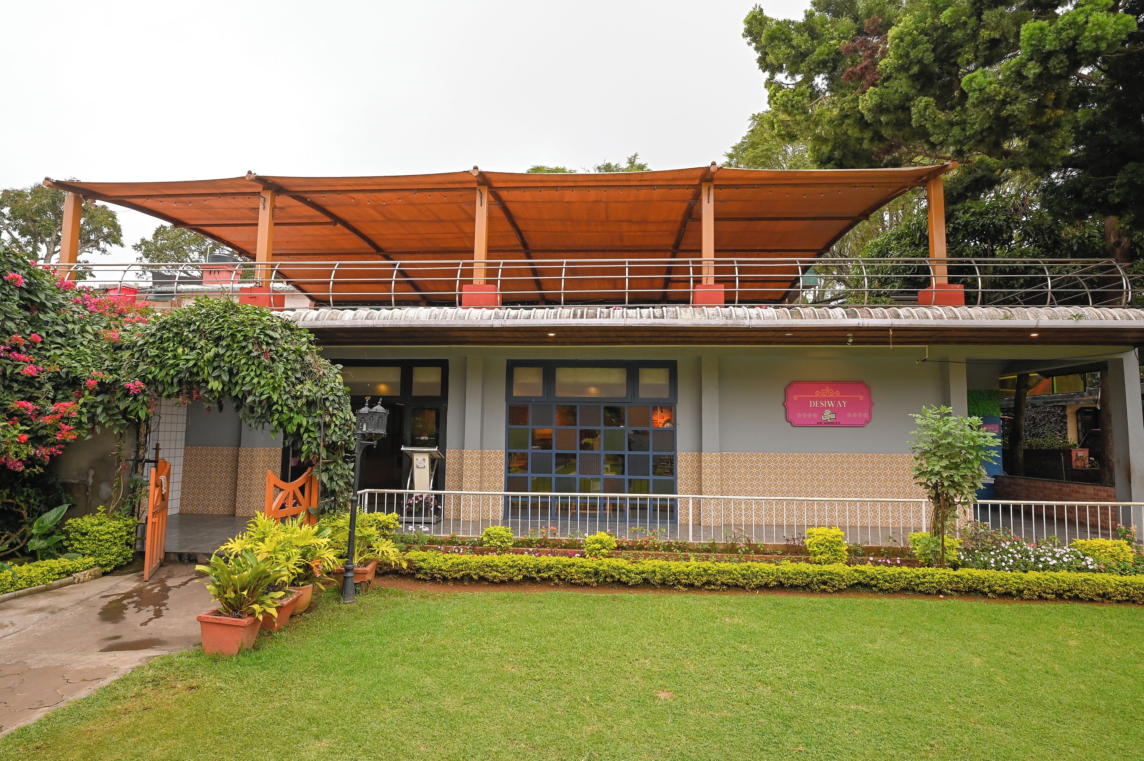 A building with a covered entrance, a signboard, and a well-maintained garden with potted plants and a small tree.