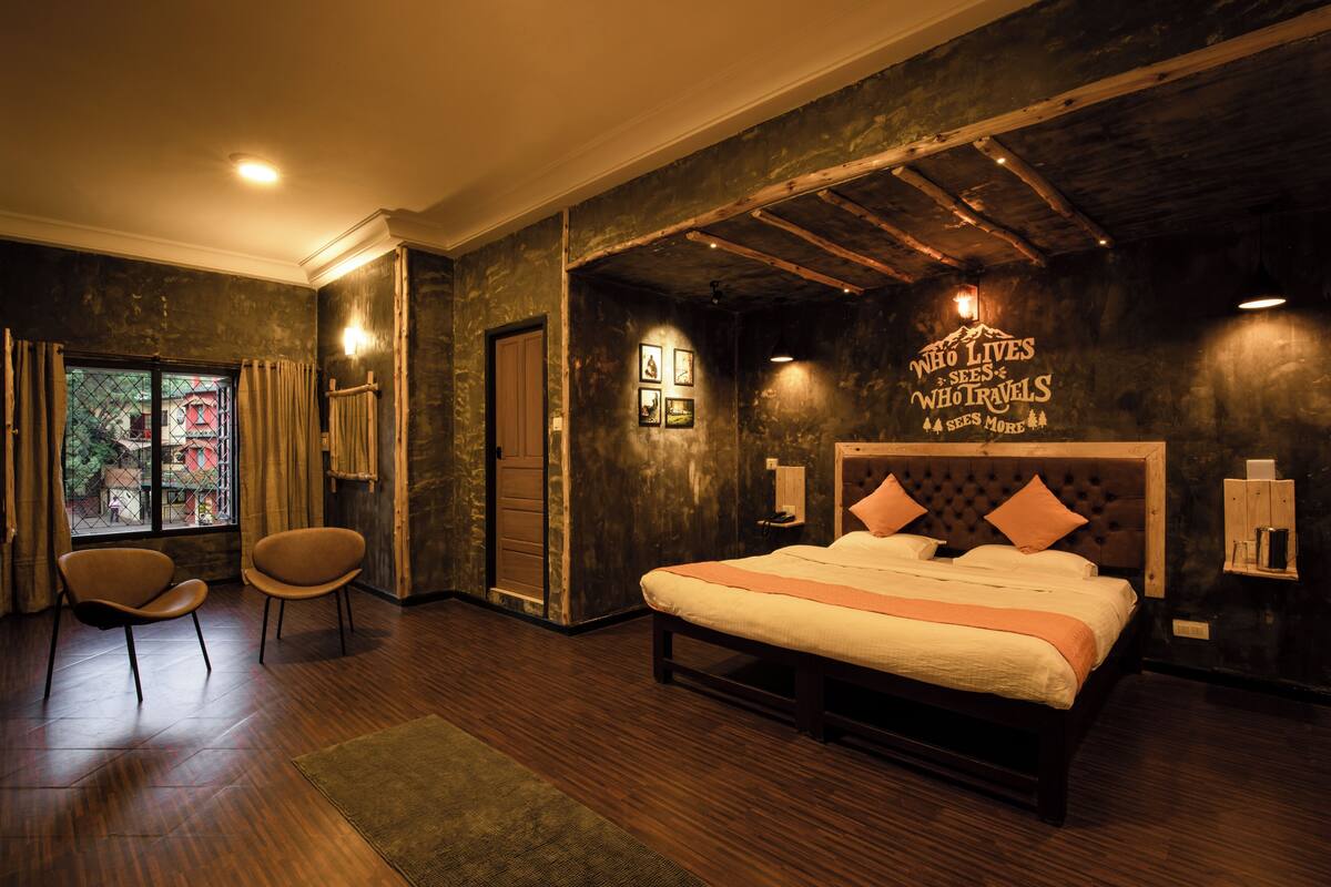 A bedroom with a large bed, two chairs, a window with curtains, and a wall with a motivational quote.