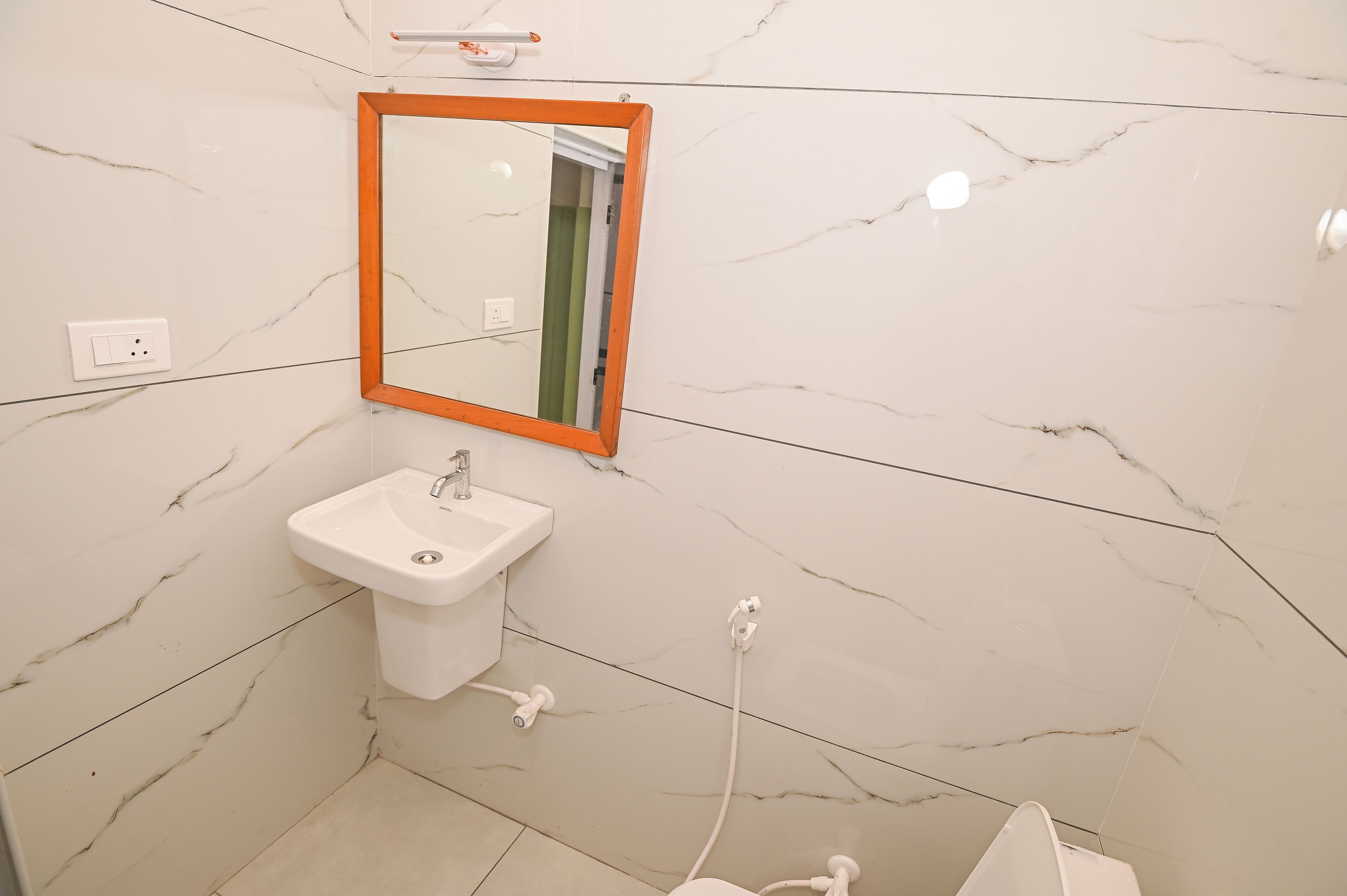 Une salle de bain avec un mur en marbre blanc, un lavabo blanc et un miroir doté d’un cadre orange.