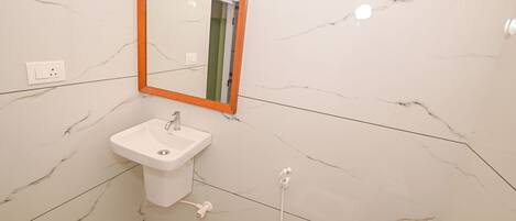 Une salle de bain avec un mur en marbre blanc, un lavabo blanc et un miroir doté d’un cadre orange.