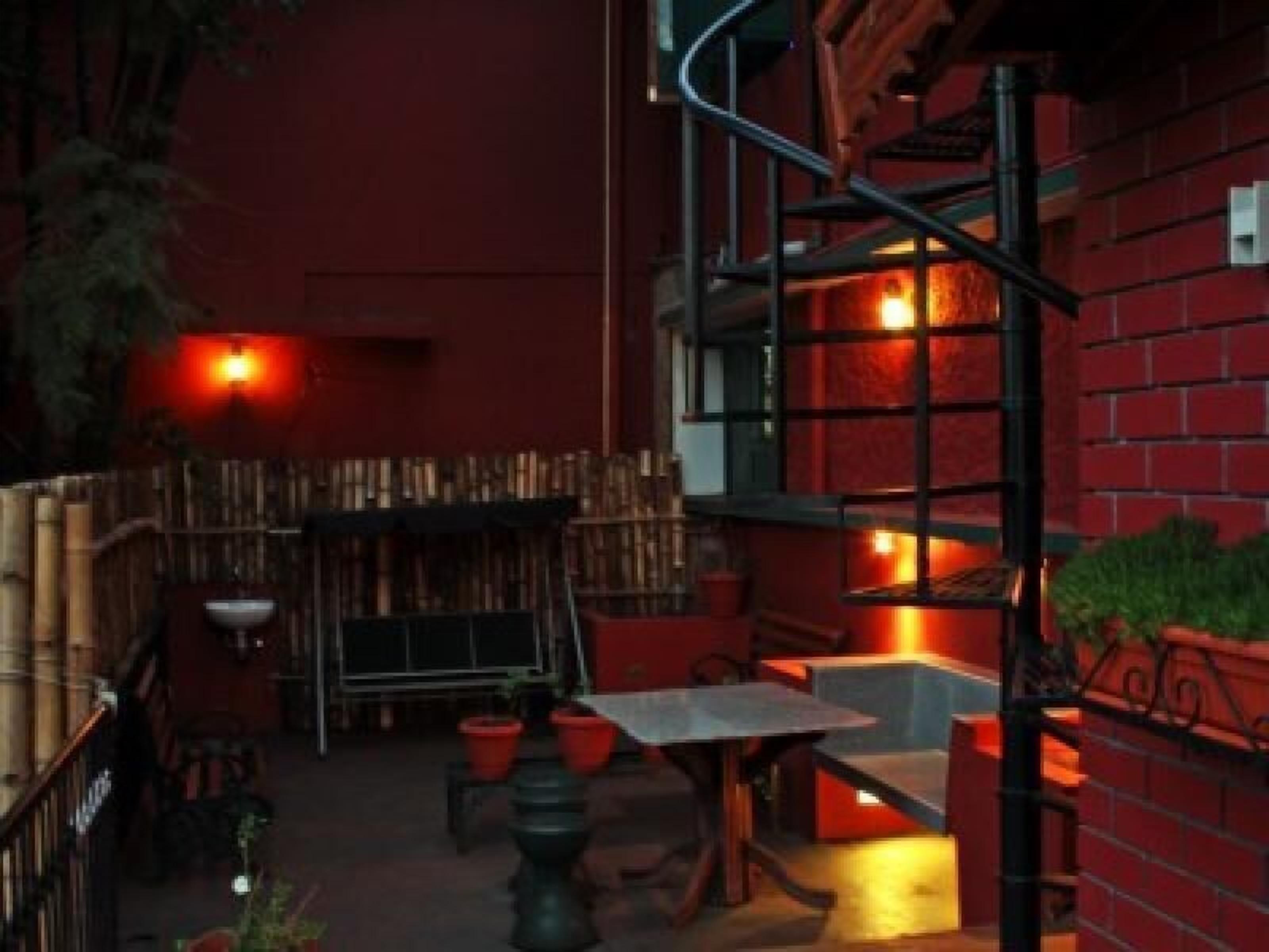 A narrow outdoor patio with a red brick wall, a metal staircase, and a table with chairs.