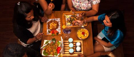 A group of people dining at a wooden table with various dishes, including a salad, rice, and a dessert.