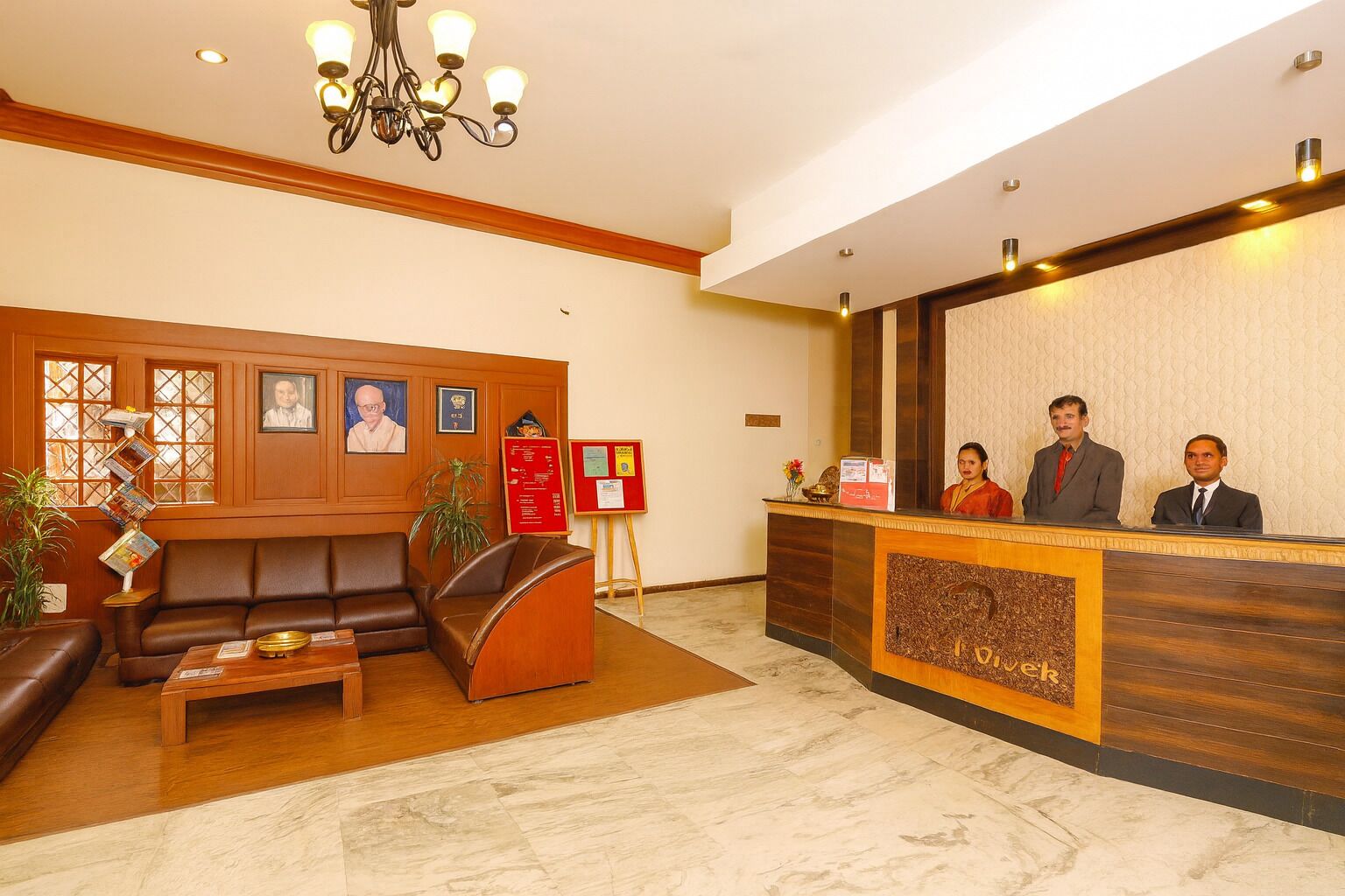 Zona de recepción de hotel con un mostrador de madera, un sofá de cuero, una mesa de centro y una araña.
