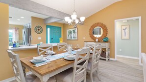 A dining area with a wooden table set for six, white chairs, a chandelier, and a mirror above the table. - HOT TUB & POOL TABLE The Coconut Lounge - Newly Renovated 3/2 in The Village of DeSoto (DeSoto, The Villages)