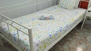 Una cama individual con colcha estampada, estructura metálica blanca y una mesita de noche con lámpara.