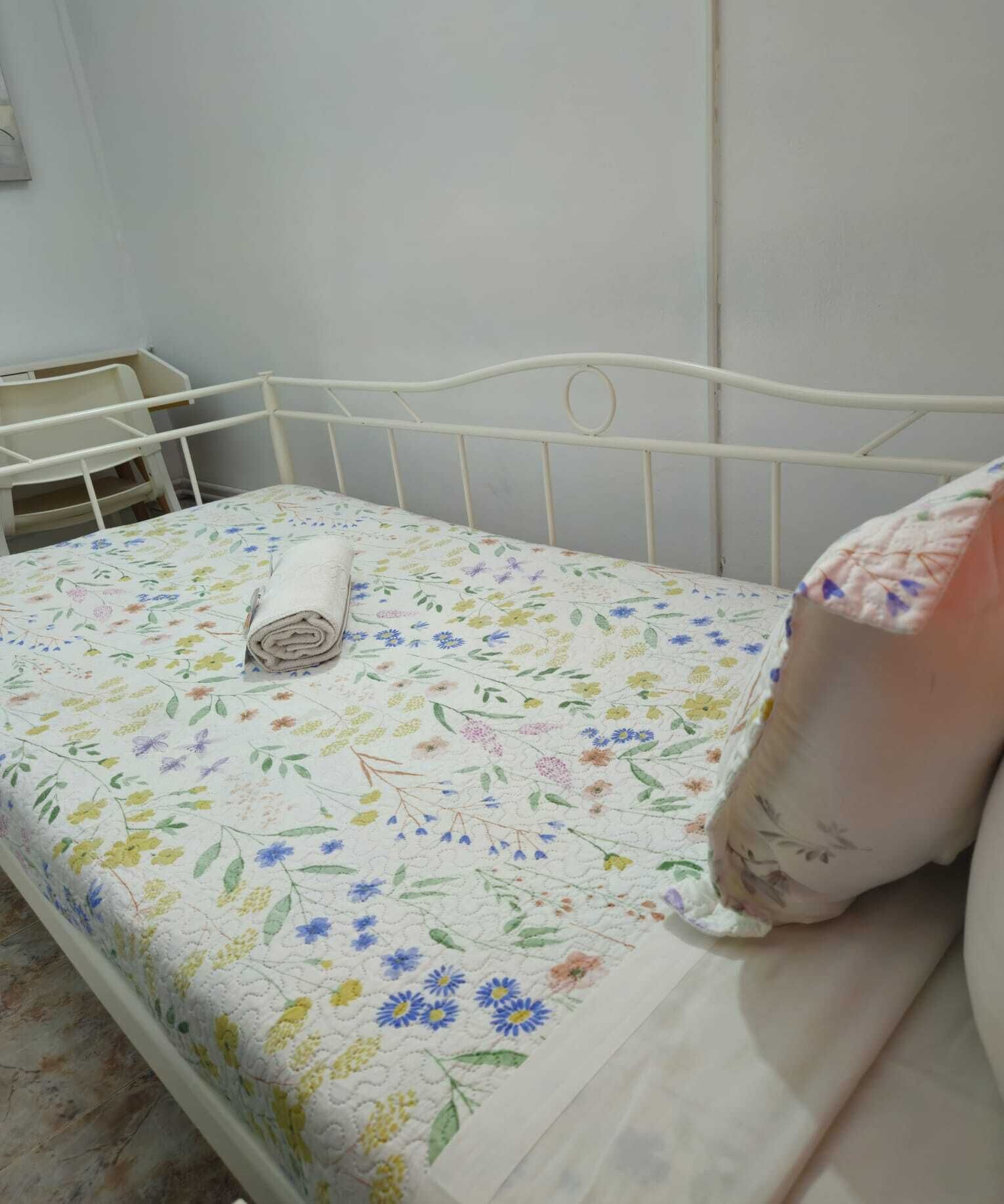 Una cama con una colcha floral, una toalla enrollada y una almohada.