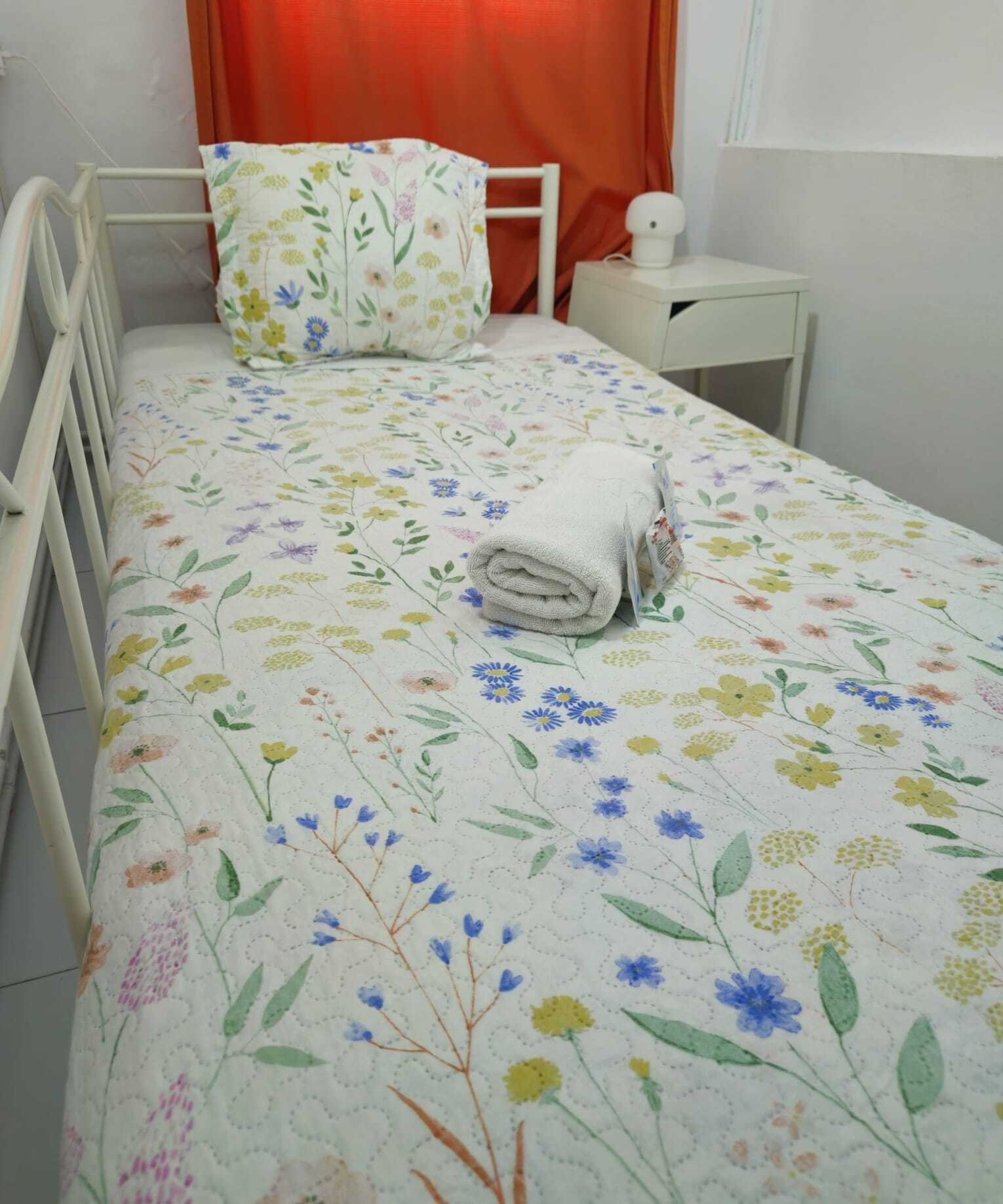 Una cama bien hecha con una colcha floral, un cabecero blanco y una mesita de noche con una lámpara.
