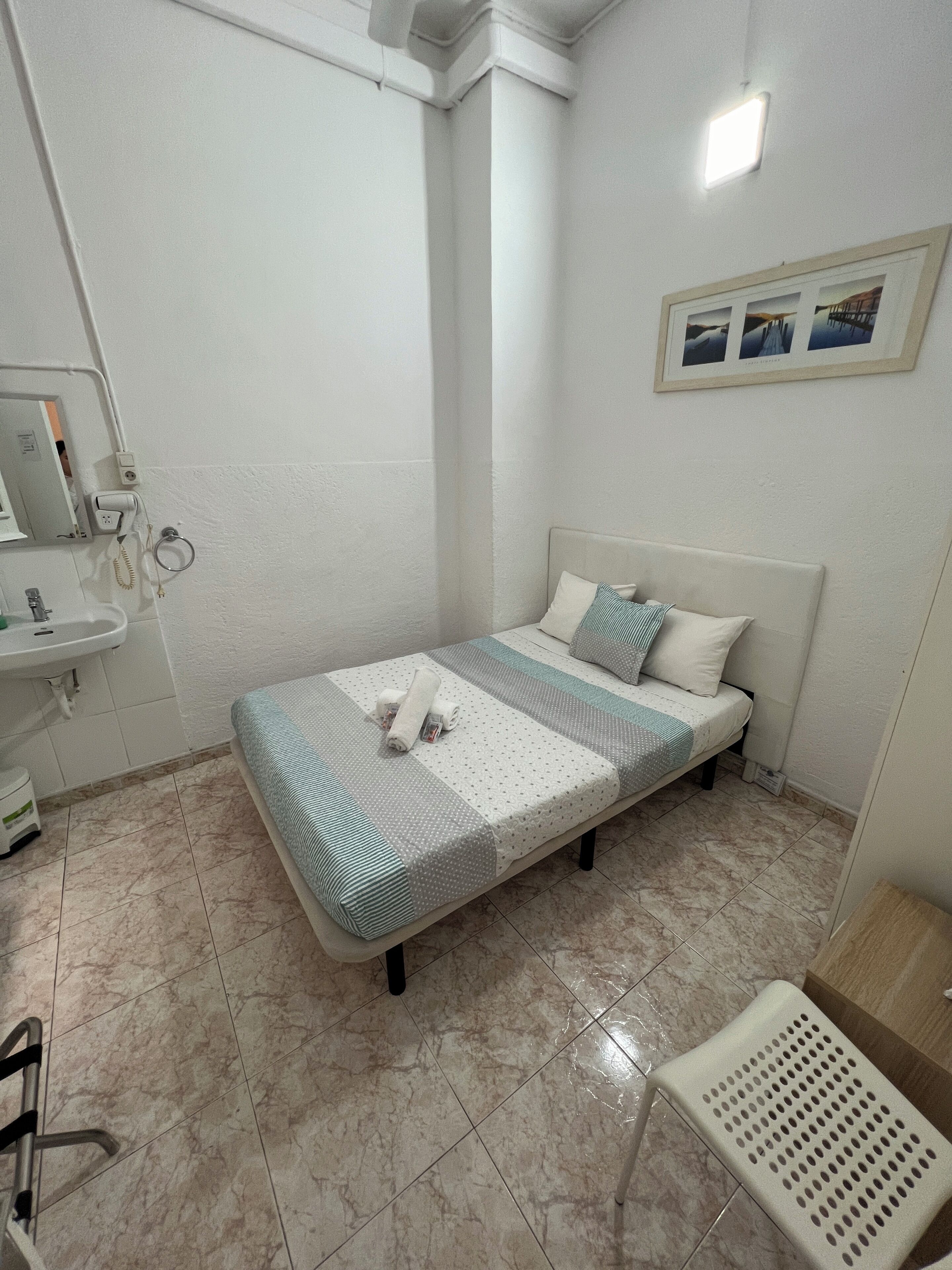 Un dormitorio pequeño y ordenado con cama, mesita de noche, lavabo y espejo.