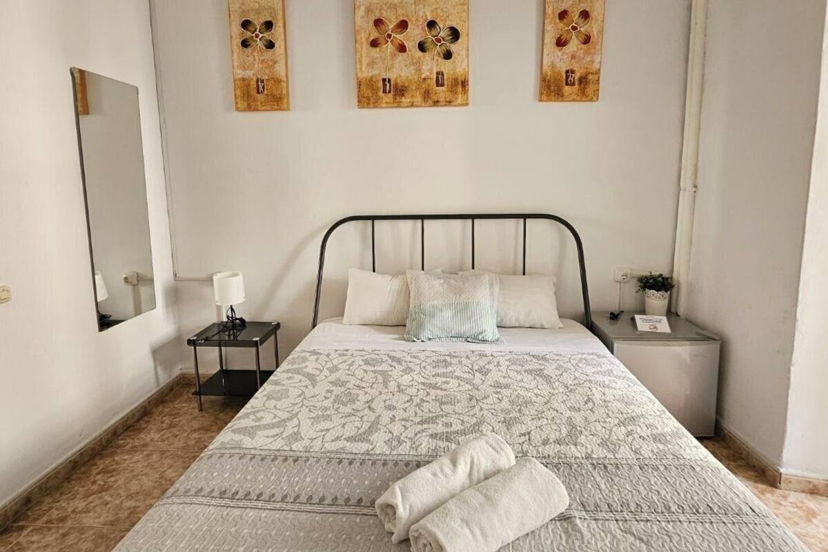A neatly made bed with a patterned bedspread and two pillows, a bedside table with a lamp, and three wall-mounted artworks above the bed.